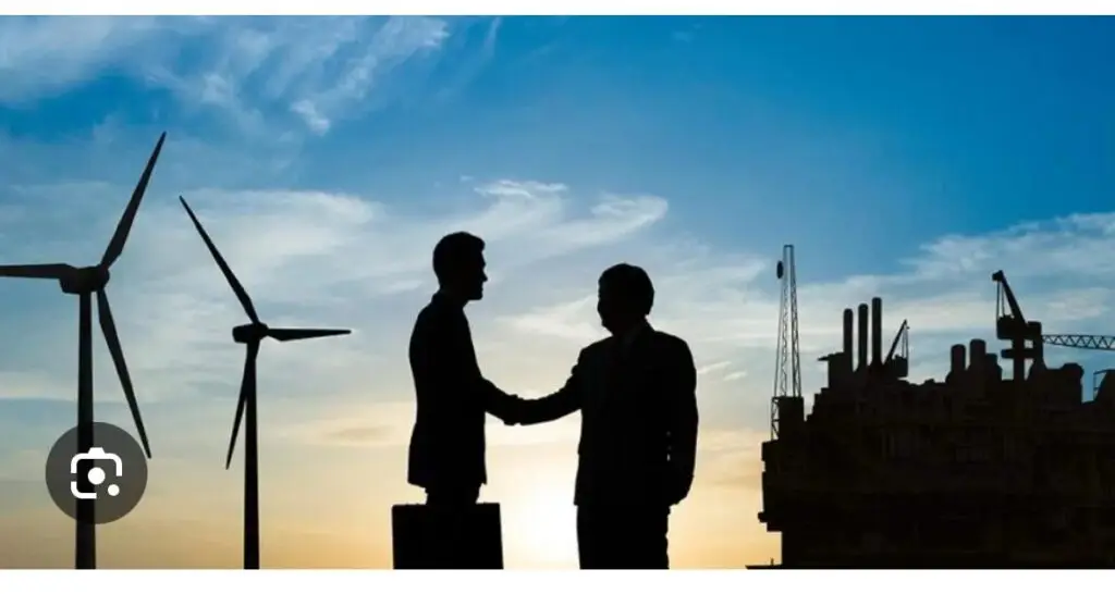 Two men shake hands in front of an offshore wind farm and oil rig, symbolising international energy cooperation.